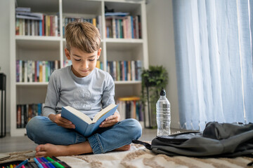 caucasian boy pupil student read book at home on the floor study learn