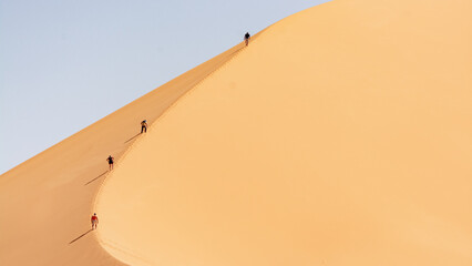 Tadrart landscape in the Sahara Desert, Algeria. Four adventurous tourists set out to climb the Ouan Zaouten dune
