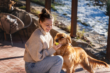 Young adult happy woman playing with her retriever dog on the terrace of a country house in early spring - 750090071