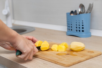 woman cutting potatoes on a kitchen board.