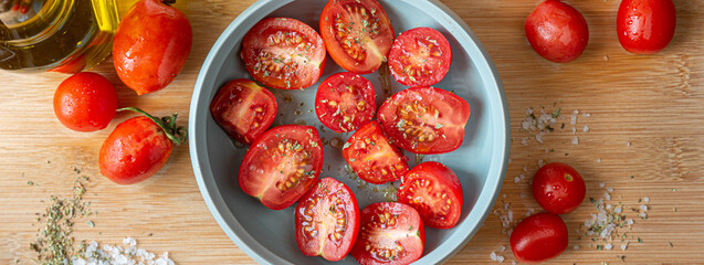Naples, Italy. Food image of a bunch of cutted organic raw tomatoes in a little turquoise bowl on a wooden cutting board with coarse salt, oregano and a glass of olive oil. Banner header image.
