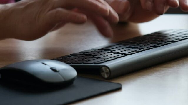 Close-up view of a persons hands typing rapidly on a black keyboard, with a wireless mouse lying adjacent on a wooden desk surface. The interaction indicates busy work or communication, possibly in an