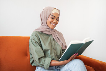 Islamic young woman in headscarf reading book at home