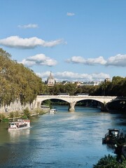 This image presents a serene view of the Tiber River flowing through Rome, Italy. A stone bridge...