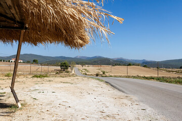 Empty asphalt road with no cars nor people, with a straw shed for shade, also clearly abandoned,...