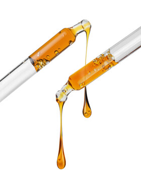 Stretched yellow oily drops drip from pipettes close up isolated on a white background