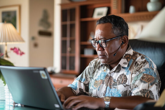 A middle aged man is seated in front of a laptop computer, focused on the screen. He is wearing glasses. The room is a well-lit home office.