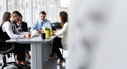 Group of diverse colleagues in formal clothing discussing business ideas while gathering at table in modern office and working together.