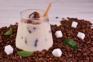 A glass of cold coffee on a background of coffee beans and sugar cubes.
