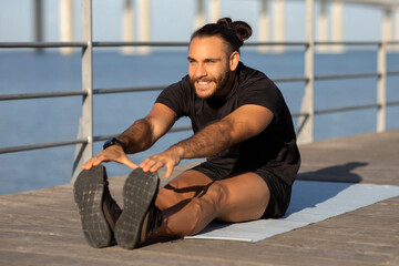 athletic guy in sportswear demonstrates seated forward bend at seaside