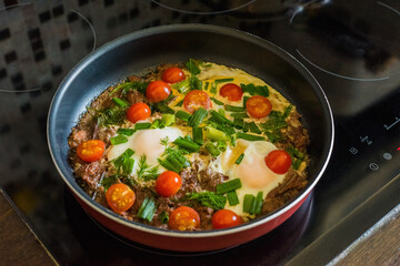 cook scrambled eggs with onions tomatoes and meat in a frying pan on an electric stove