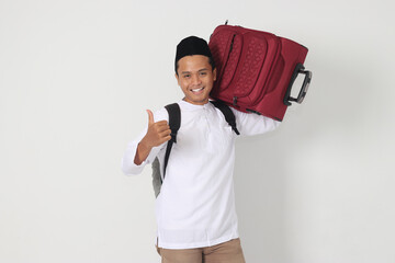 Portrait of attractive Asian muslim man carrying suitcase while showing thumbs up hand gesture and...