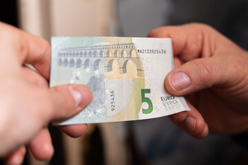 concetto di scambio di denaro. visuale in primo piano sulle mani di due persone caucasiche che si scambiano una banconota da 5 euro