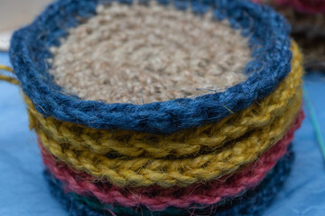 A set of round crocheted jute coasters or washcloths of different colors lie in a stack on a blue background.