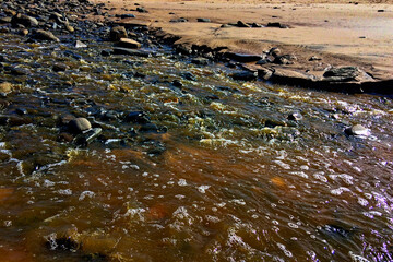 Water flows among stones on a rocky surface, reflecting light and creating a dynamic scene.