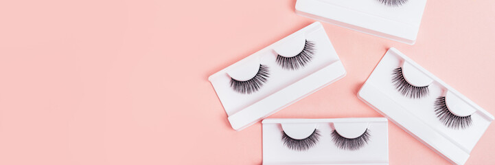 Different fake eyelashes in boxes on trendy pastel pink background. Makeup accessories. cosmetics...