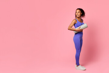 Athletic black lady holding foam roller standing on pink background