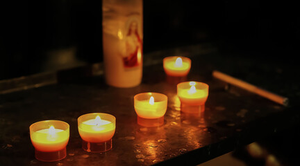 Closeup of isolated few single sacrificial candles in catholic church, blurred jesus symbol  candle...