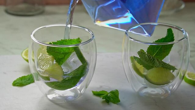 Summer drink pouring, iced organic blue and violet butterfly pea flower tea with mint and lime