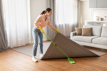 Focused woman lifting rug to clean underneath with mop