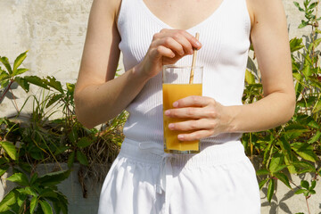 a young woman holds a glass of orange juice and a paper tube in front of her. the concept of summer...
