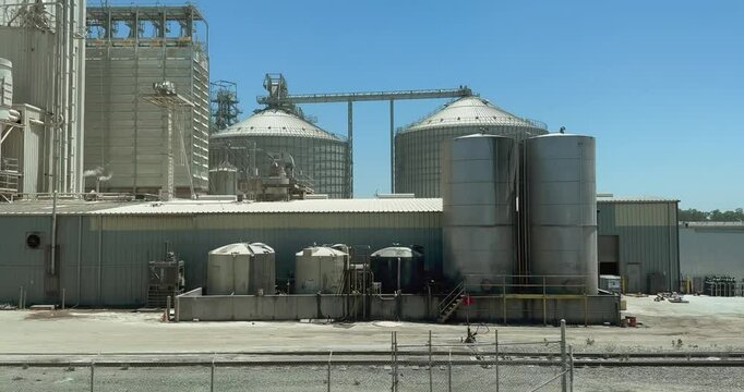 A panning shot of agricultural storage in the San Joaquin Valley. Train tracks, trucks, freight containers, boxcars, massive silos, steel framing, and other details express business and industry.