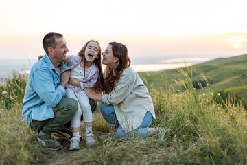 Mom, dad and child are happy walking at sunset. The concept of a happy family. Little girl is...