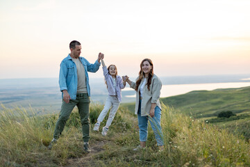 Mom, dad and child are happy walking at sunset. The concept of a happy family. Parents hold the child's hands. Summer concept. People spend time outdoor in summer