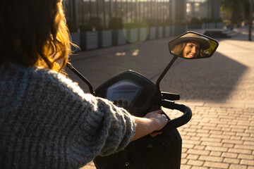 Woman tourist on a four wheel mobility electric scooter on a city street. The woman's face is visible in the rearview mirror..