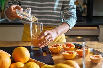 Female hands making homemade grapefruit juice with hand citrus juicer. Anonymous woman pouring...