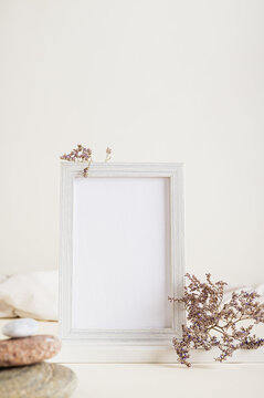 Empty photo frame, dried flowers and stones on a light background vertical view