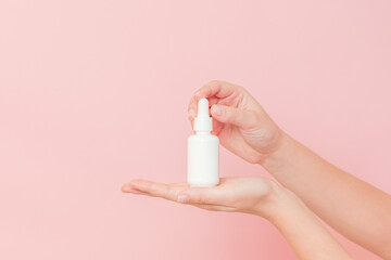 Glass cosmetic bottle for serum (hyaluronic acid and collagen) in hand on pink background. Beauty concept