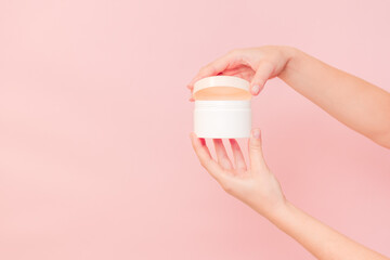 Round jar of cosmetic cream in hand on pink background. Cosmetics beauty mockup for product branding