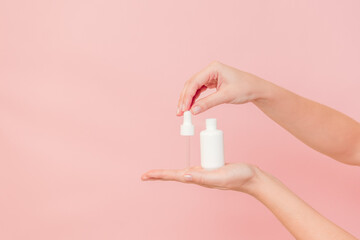 White tube with pipette with serum lotion or essential oil (hyaluronic acid and collagen) in hands on pink background. Skin care cosmetics concept, beauty flyer