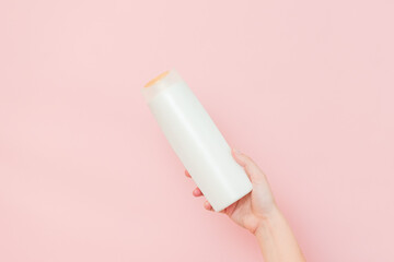 Hands holding shampoo, hair conditioner or body lotion bottle in pink background. Cosmetics bottle