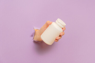 Cool view on white bottle plastic tube in hands on lilac background. Packaging for pills, capsules or supplements. Cosmetics