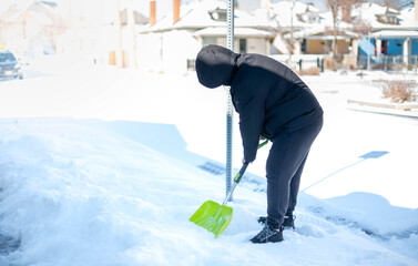 A man in a warm black jacket and trousers shoveling snow in front of their home for prepare the road for convenience.