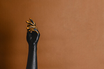 Elegant woman's hands with black and gold painted on her skin on brown background. High Fashion art...