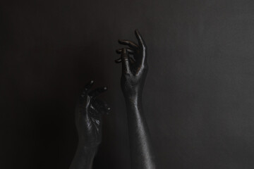 Naklejka premium Woman's hands with black paint on her skin on dark background. High Fashion art concept