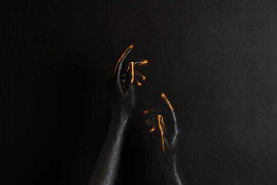 Woman's hands with black and gold paint on her skin on dark background. High Fashion art concept