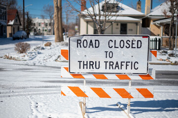 Road closed sign bars traffic from snow covered road in the winter season and winter snow storm.