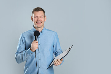 Male journalist with microphone and clipboard on grey background. Space for text