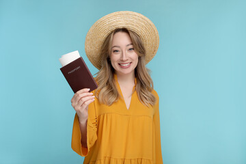 Happy young woman with passport, ticket and hat on light blue background