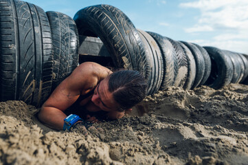 Woman participating in an OCR race while crawling out of a car tires tunnel