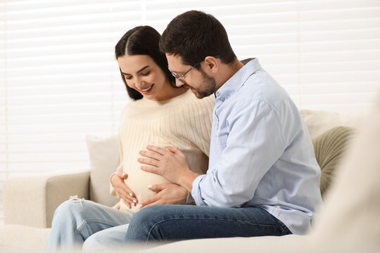 Happy pregnant woman spending time with her husband on sofa at home