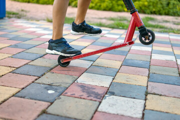 A close-up shot in the park focuses on a boy's feet and his scooter, capturing the essence of outdoor play and youthful joy