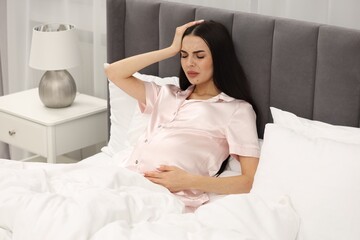 Pregnant woman suffering from headache in bed at home