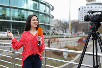 Young female journalist with microphone working on city street
