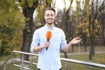 Young male journalist with microphone working in park