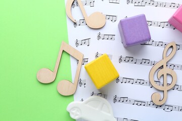 Wooden notes, music sheets and toys on light green background, top view with space for text. Baby...